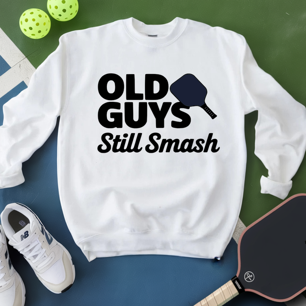 White sweatshirt with 'Old Guys Still Smash' text, pickleball paddle, and balls on a green and blue background