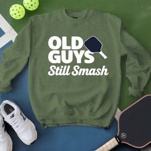 Green sweatshirt with 'Old Guys Still Smash' text, pickleball paddles, and balls on a green and blue background