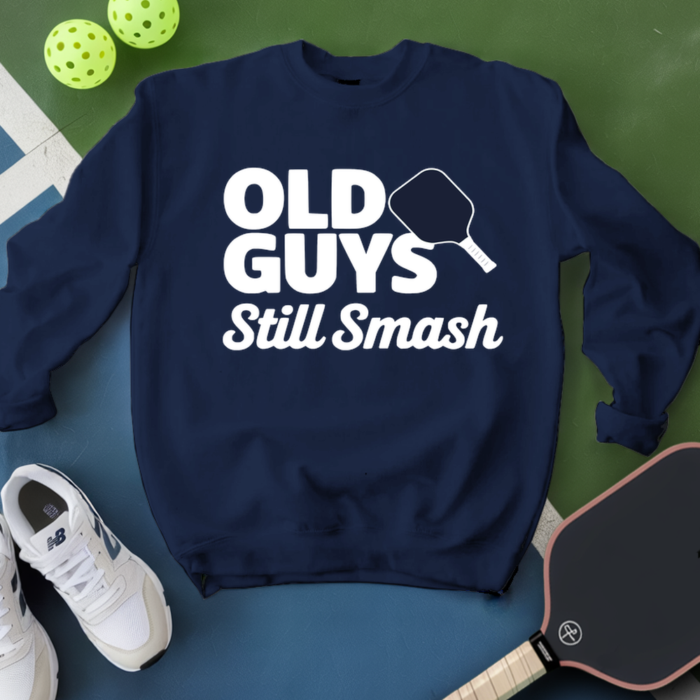 Navy blue sweatshirt with 'Old Guys Still Smash' text, white sneakers, and pickleball equipment on a green and blue background.