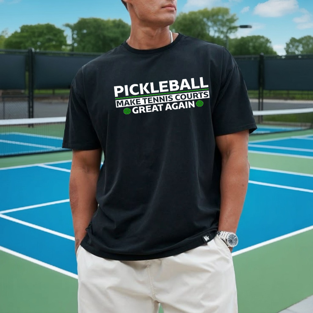 Person wearing a black t-shirt with pickleball-themed text on a tennis court.