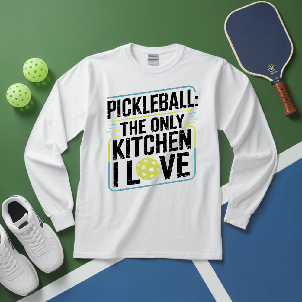 White long-sleeve shirt with pickleball-themed text on a green and blue surface with pickleballs and a paddle.