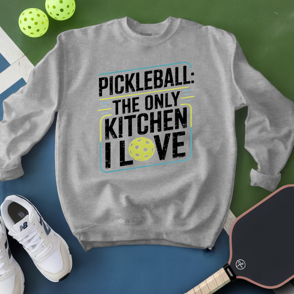 Gray sweatshirt with pickleball-themed text, surrounded by pickleballs and a paddle on a green and blue background.