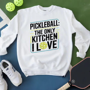 White sweatshirt with pickleball-themed text, shoes, and paddle on a green and blue background