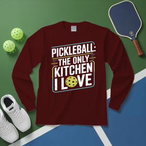 Maroon long-sleeve shirt with pickleball-themed design on a green and blue surface with pickleballs and a paddle.