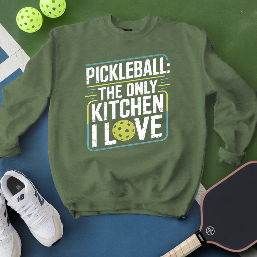 Green sweatshirt with pickleball-themed text, surrounded by pickleballs and a paddle on a green and blue background.