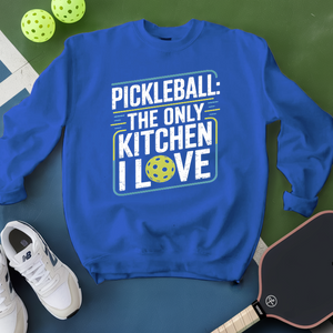 Blue sweatshirt with pickleball-themed text on a green surface with pickleballs and a paddle.
