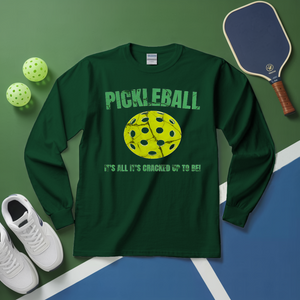 Green long-sleeve shirt with pickleball design and text on a green and blue surface with pickleball equipment.