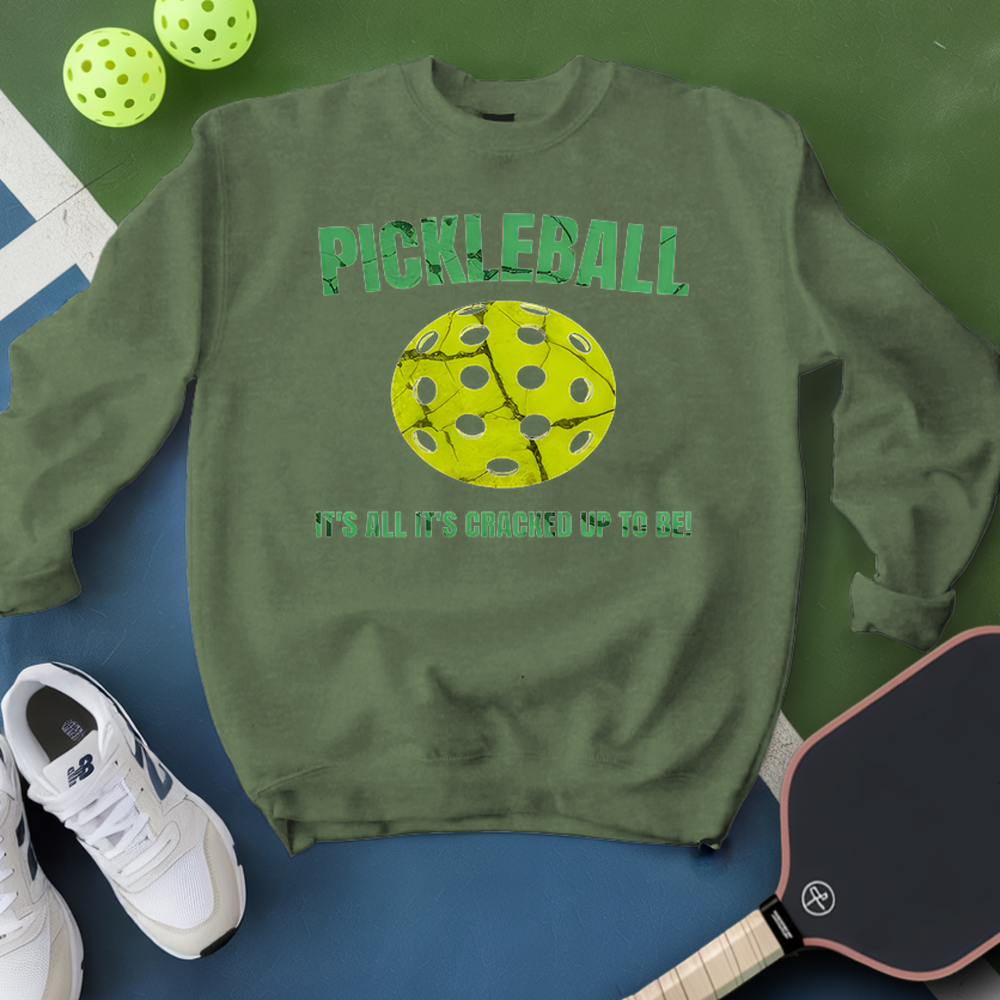 Green sweatshirt with pickleball design and text, surrounded by pickleballs and a paddle on a green and blue background.
