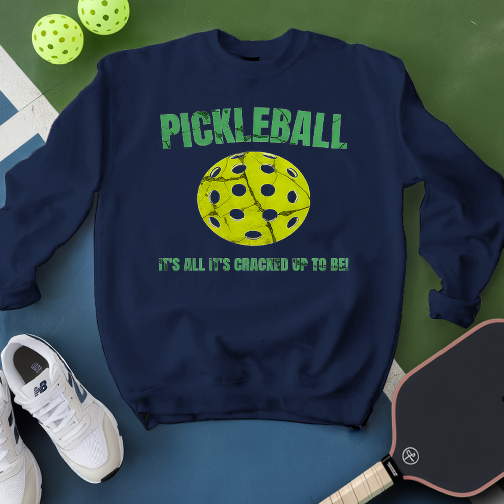 Navy sweatshirt with pickleball graphic and text, surrounded by pickleballs and a paddle on a green and blue background.