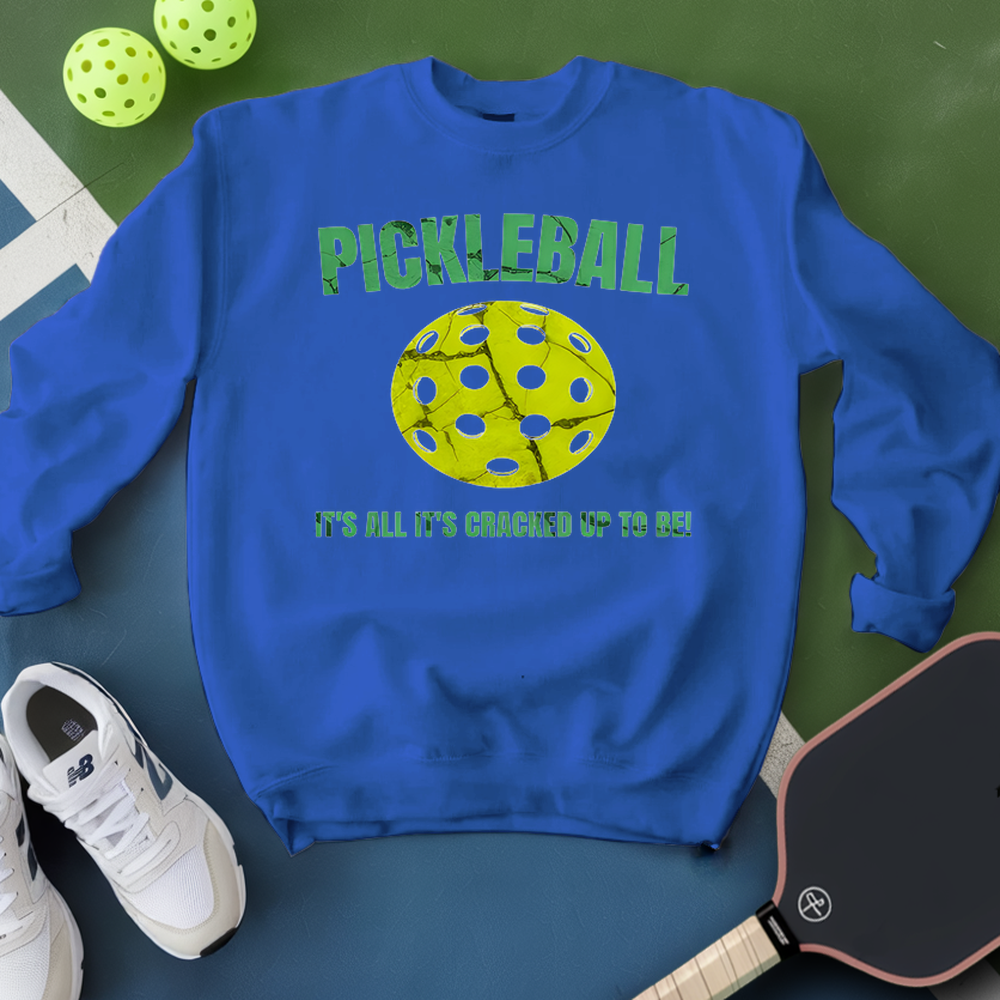 Blue sweatshirt with pickleball design and text on a green surface with pickleballs and a paddle.