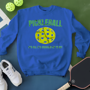 Blue sweatshirt with pickleball design and text on a green surface with pickleballs and a paddle.