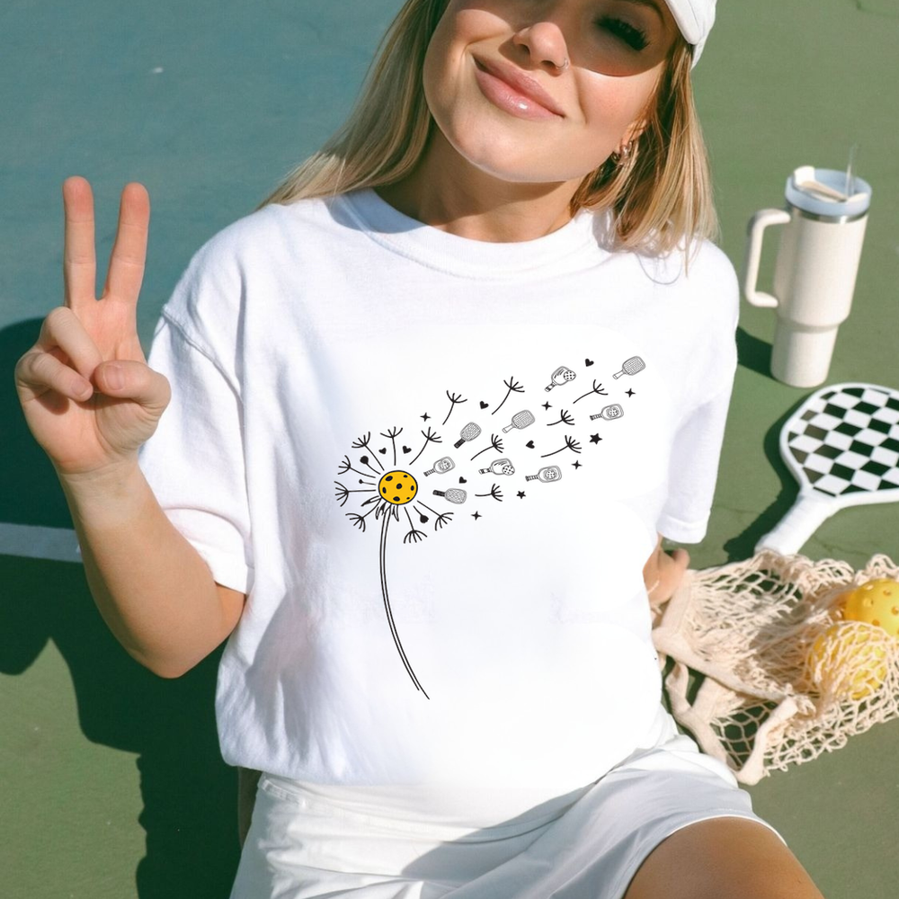Woman wearing a white t-shirt with a dandelion graphic, making a peace sign.