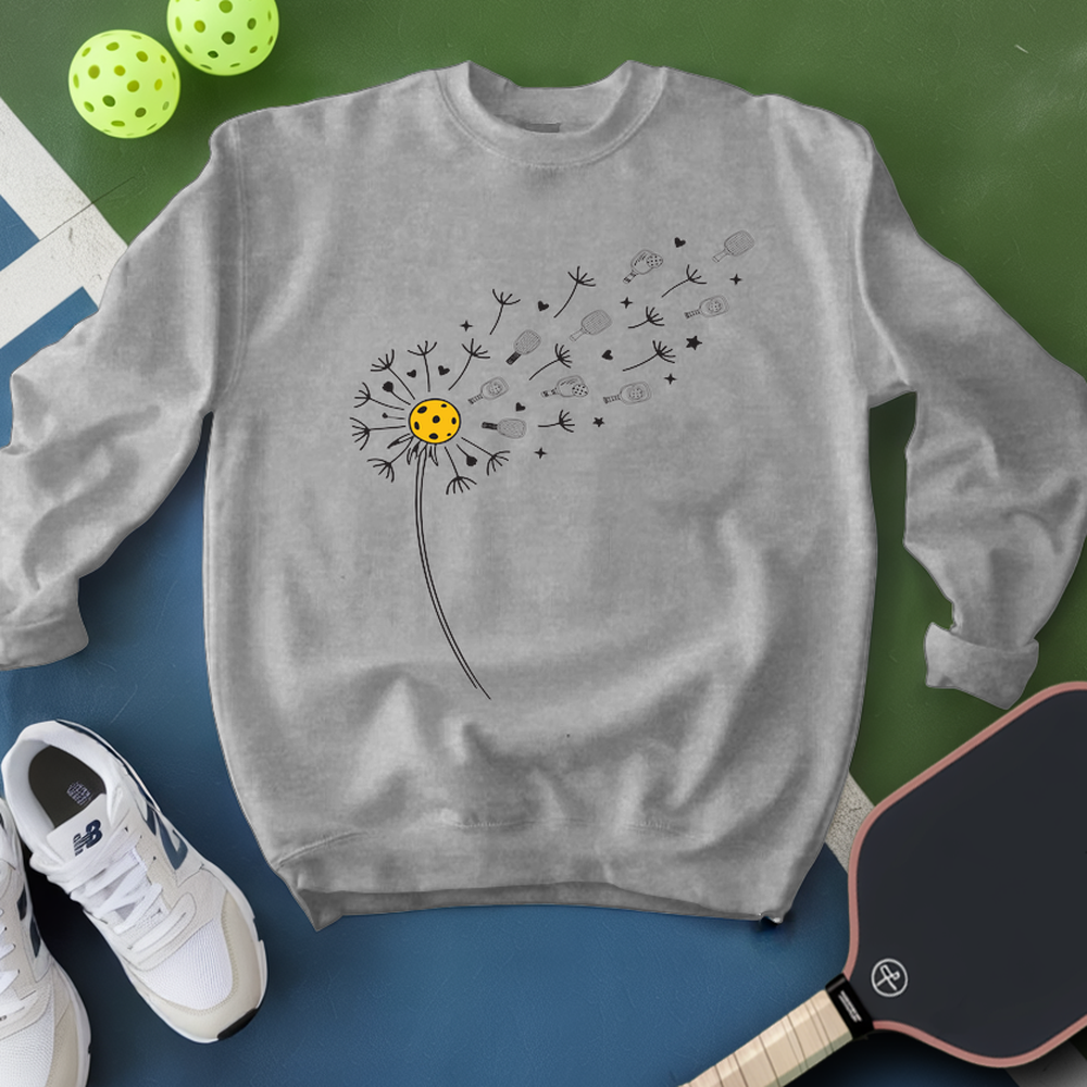 Gray sweatshirt with a dandelion graphic on a green and blue surface with pickleballs and shoes.