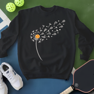Black sweatshirt with a dandelion graphic on a blue surface with pickleball equipment.