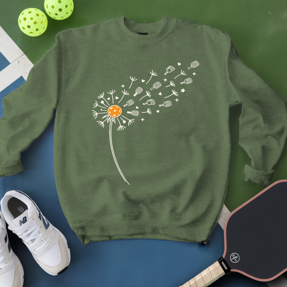 Green sweatshirt with dandelion design on a blue surface with pickleball equipment.