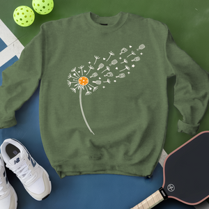 Green sweatshirt with dandelion design on a blue surface with pickleball equipment.