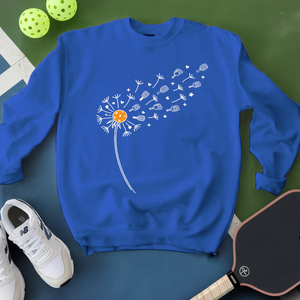 Blue sweatshirt with a dandelion graphic on a green surface with pickleballs and a paddle.