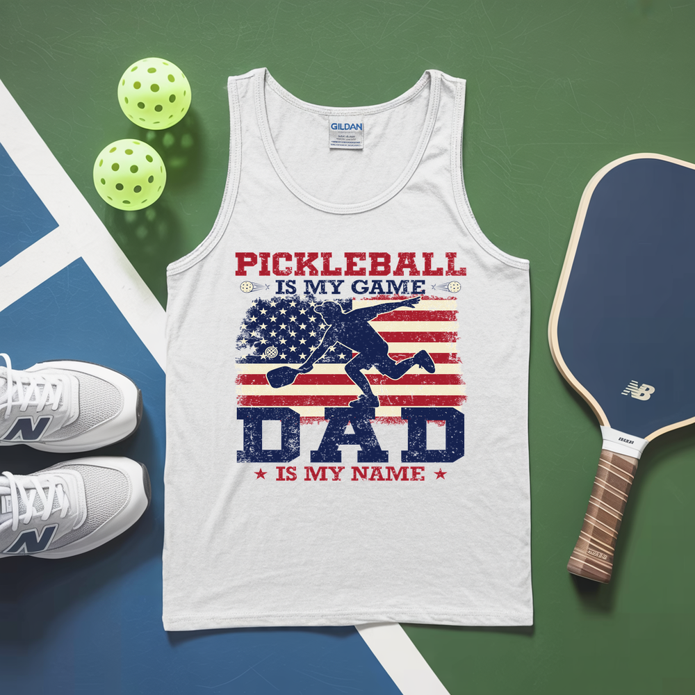 White tank top with pickleball design and text, surrounded by pickleballs and a paddle on a green and blue surface.