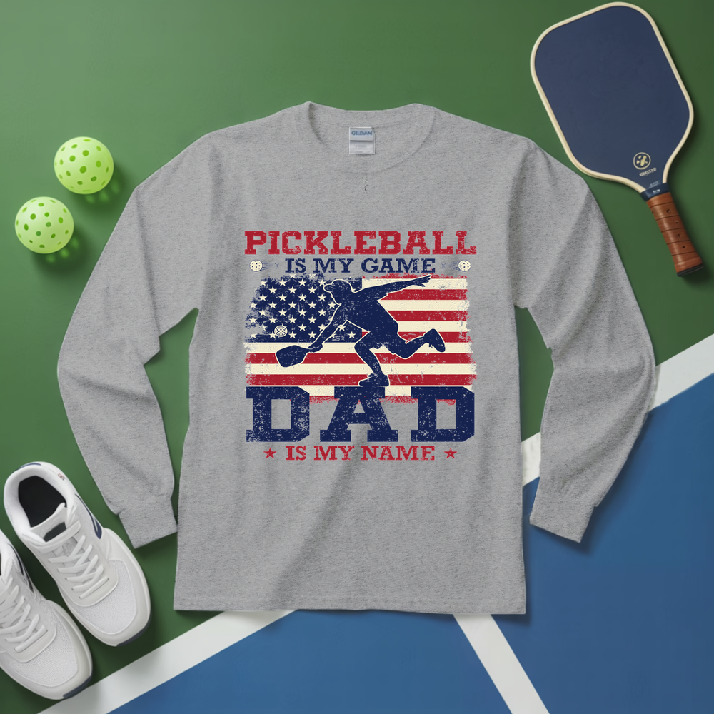 Gray long-sleeve shirt with pickleball design on a green and blue background with pickleball equipment.