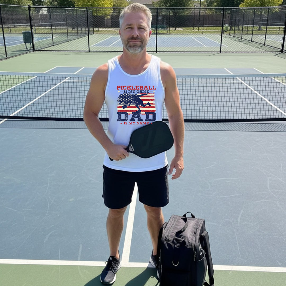 Man on a pickleball court wearing a tank top with 'Pickleball is my game, Dad is my name' text.