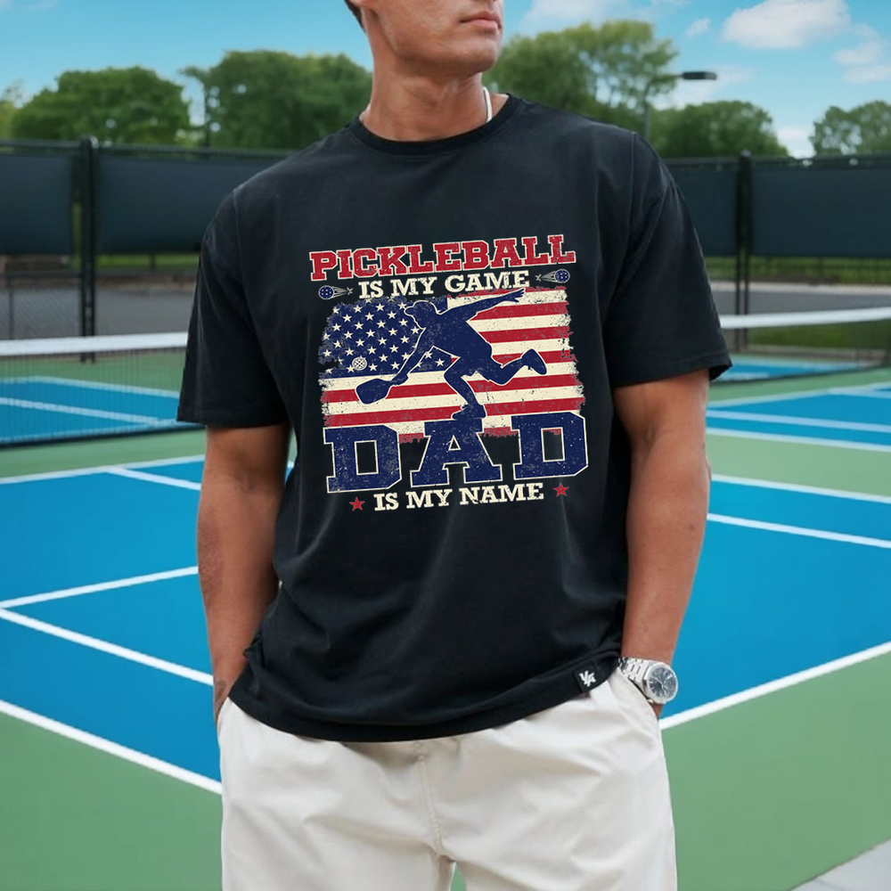 Person wearing a black t-shirt with pickleball-themed design on a tennis court.