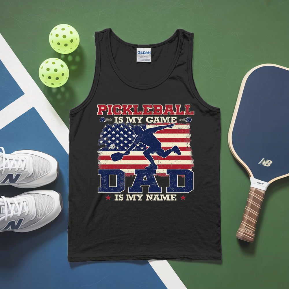 Black tank top with pickleball design and text, surrounded by pickleballs and a paddle on a green and blue surface.