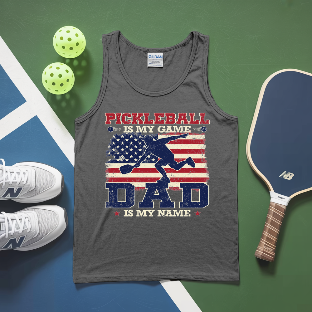 Gray tank top with pickleball design and text, surrounded by pickleballs and a paddle on a green and blue surface.