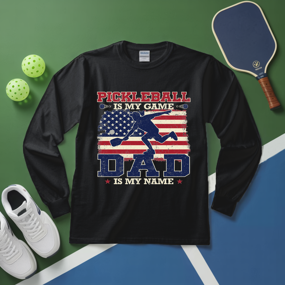 Black long-sleeve shirt with pickleball design on a green and blue surface with pickleball equipment.