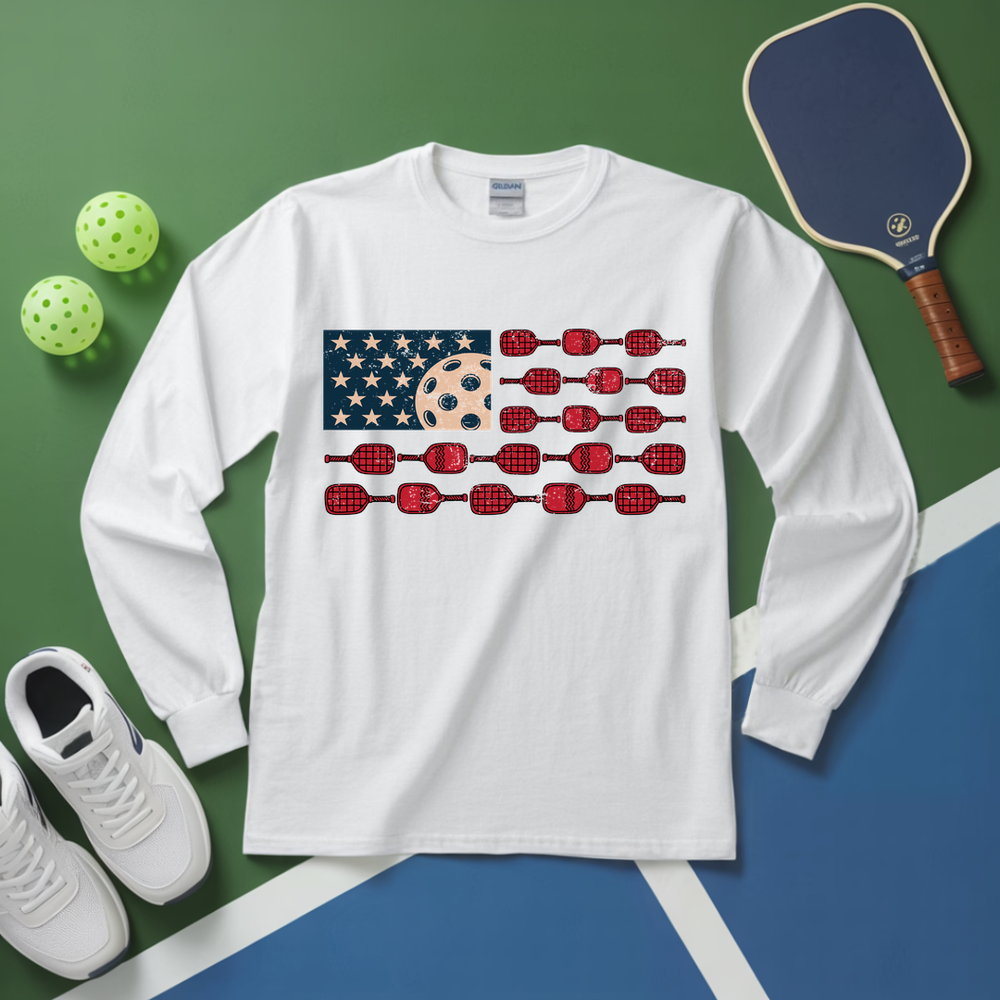 White long-sleeve shirt with American flag design featuring pickleball elements on a green and blue surface.