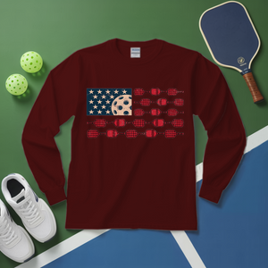 Maroon long-sleeve shirt with American flag and paddle graphic on a green and blue surface with pickleball equipment.