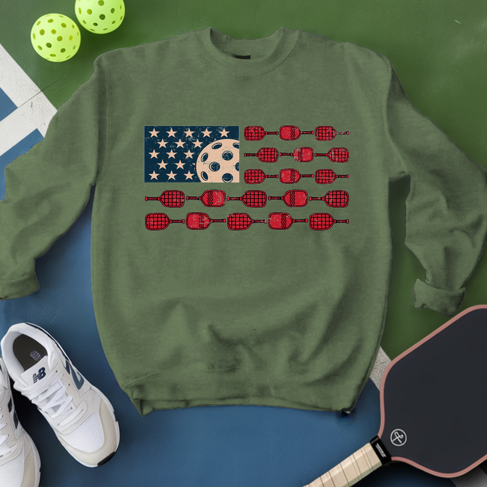 Green sweatshirt with pickleball design on a blue and green background with pickleballs and paddle.
