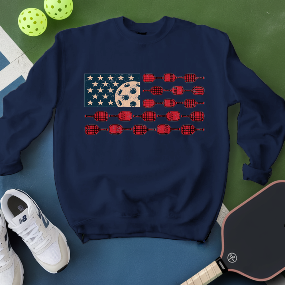 Navy blue sweatshirt with pickleball design on a green and blue surface with pickleballs and a paddle.