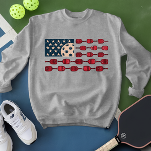 Gray sweatshirt with American flag design featuring darts and a pickleball ball, surrounded by pickleballs and a paddle.