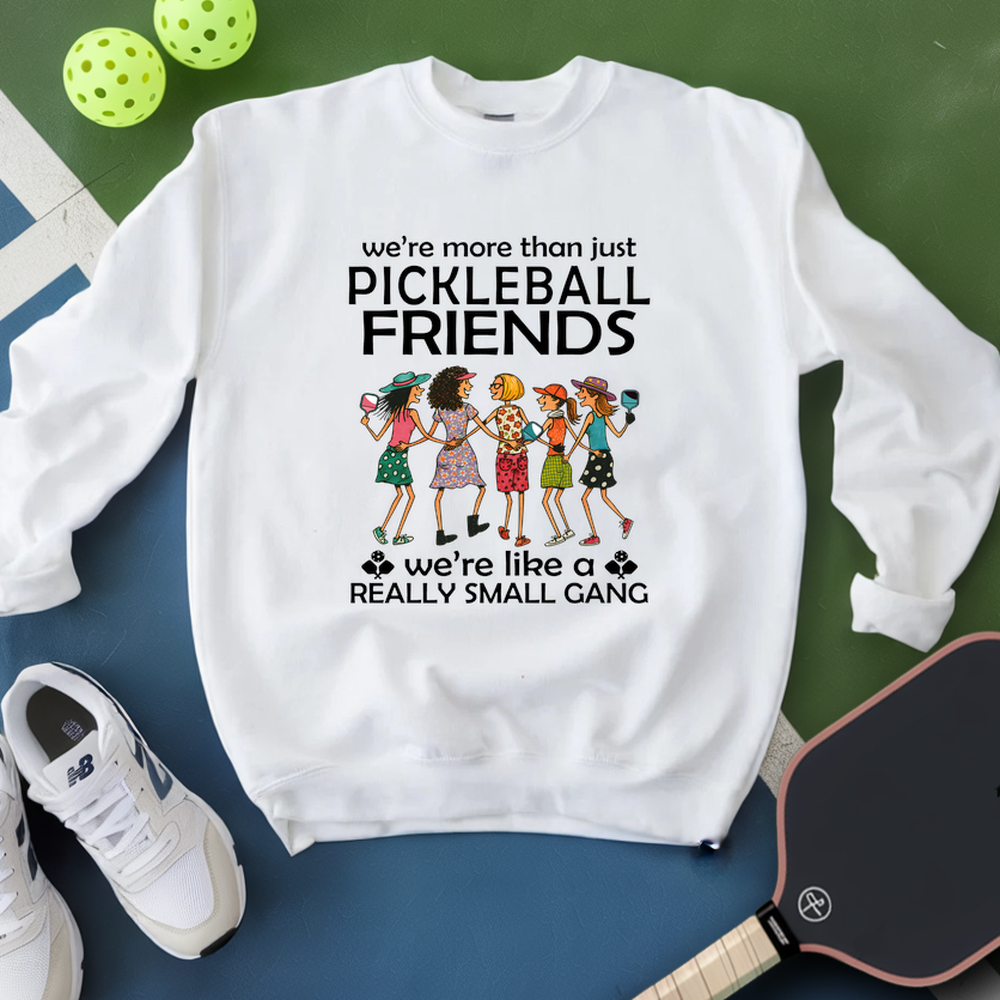 White sweatshirt with pickleball-themed design on a green and blue surface with pickleballs and a paddle.
