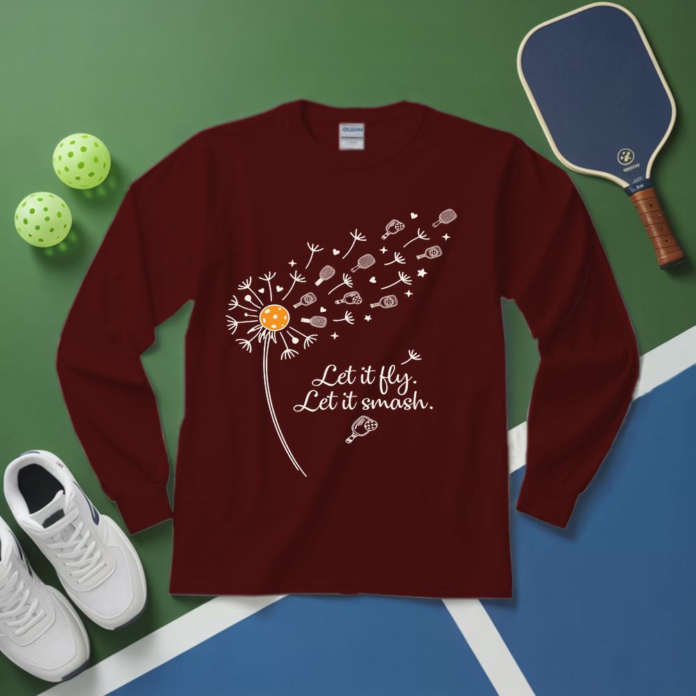 Maroon long-sleeve shirt with dandelion graphic and text on a green and blue surface with pickleballs and a paddle.