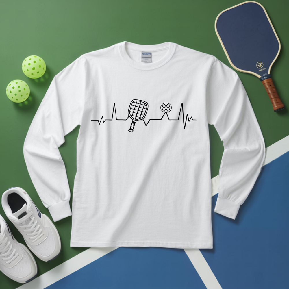 White long-sleeve shirt with pickleball design on a green and blue surface with pickleball equipment.