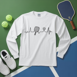 White long-sleeve shirt with pickleball design on a green and blue surface with pickleball equipment.