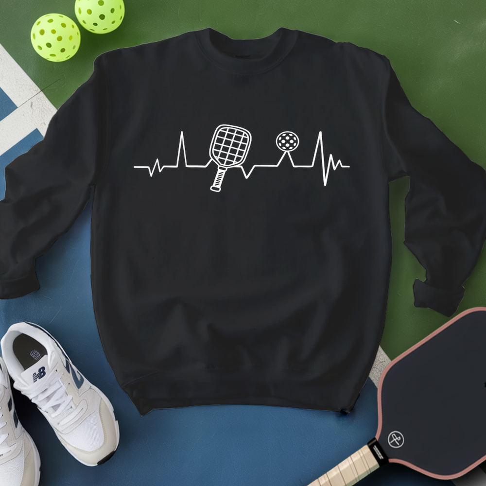Black sweatshirt with pickleball design, white sneakers, and pickleballs on a green and blue background