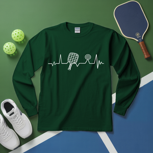 Green long-sleeve shirt with pickleball design on a green and blue surface with pickleballs and a paddle.