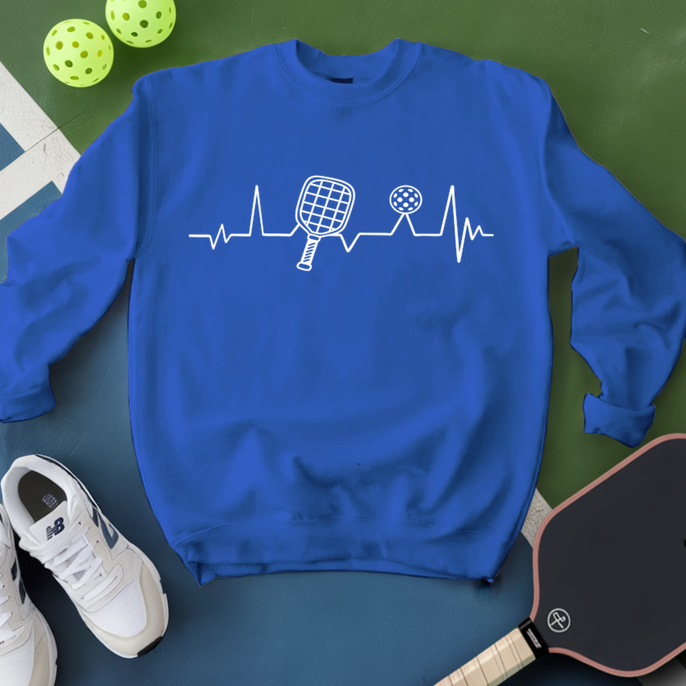 Blue sweatshirt with pickleball design on a green surface with pickleballs and a paddle.
