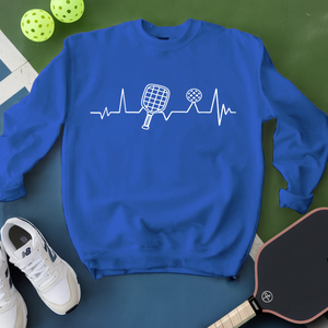 Blue sweatshirt with pickleball design on a green surface with pickleballs and a paddle.