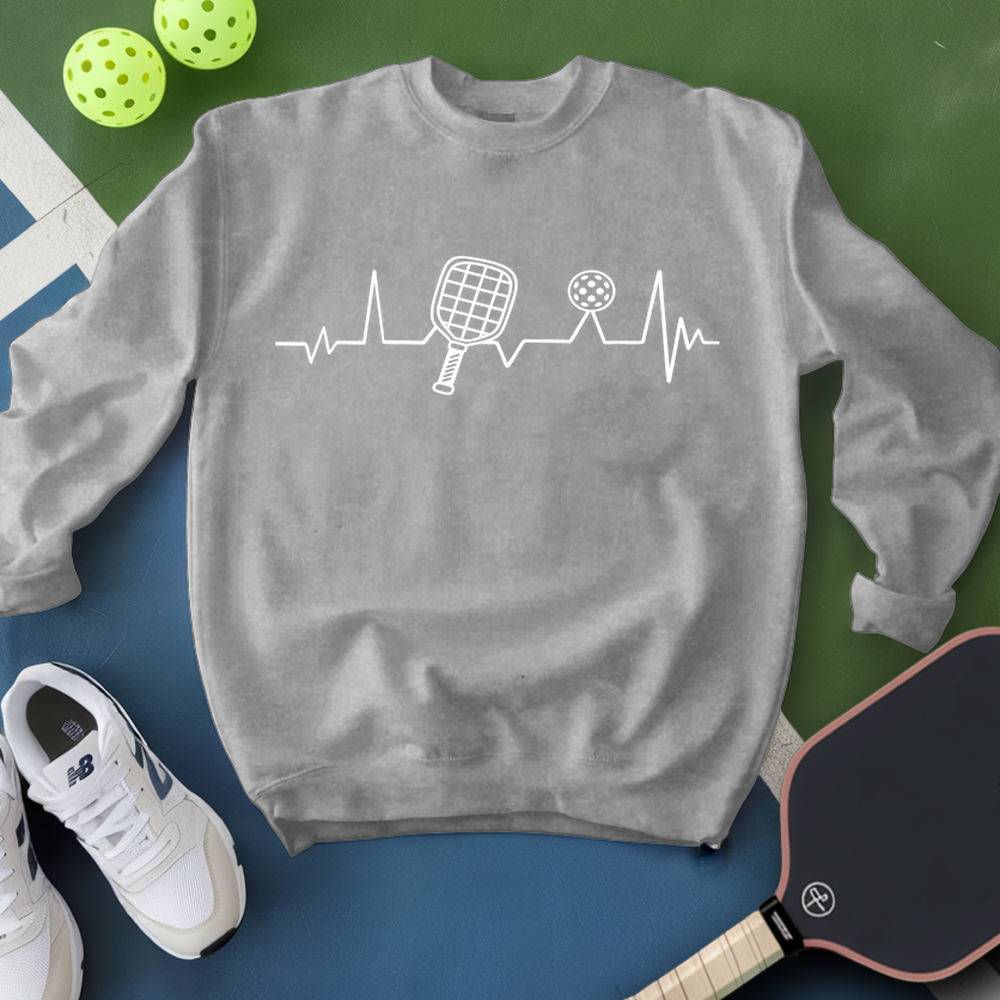 Gray sweatshirt with pickleball design, surrounded by pickleballs and a paddle on a green and blue background