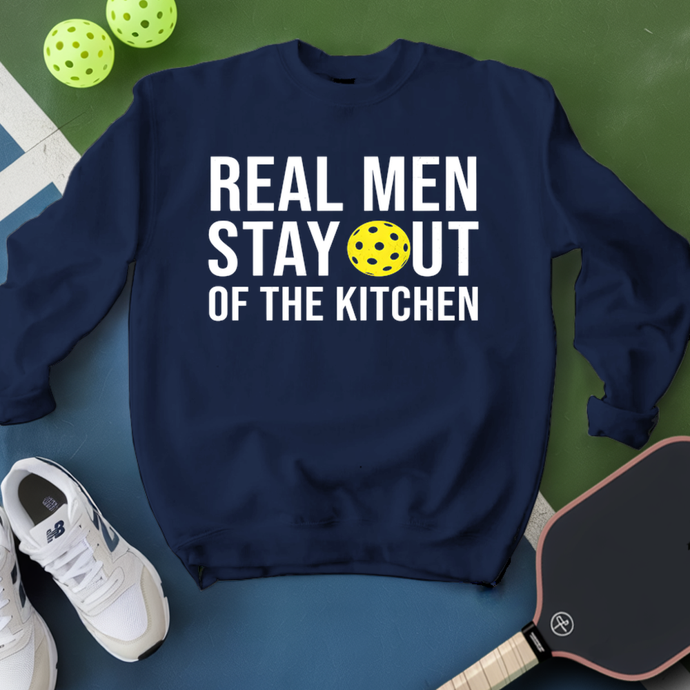 Navy blue sweatshirt with 'Real Men Stay Out of the Kitchen' text and pickleball ball, paddle, and shoes on a green and blue background.
