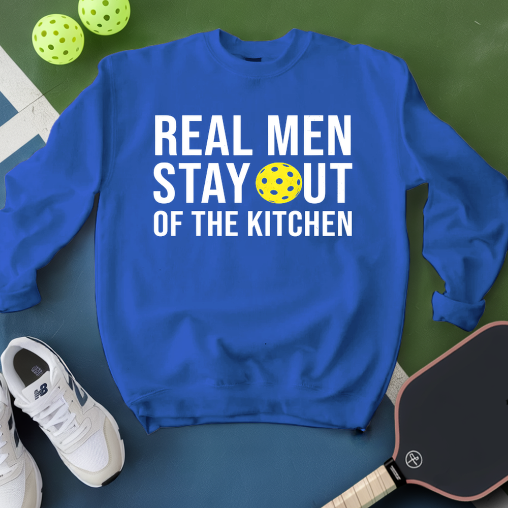 Blue sweatshirt with 'Real Men Stay Out of the Kitchen' text and pickleball ball on a green surface.