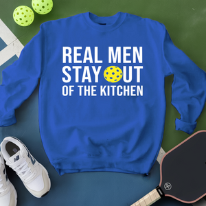 Blue sweatshirt with 'Real Men Stay Out of the Kitchen' text and pickleball ball on a green surface.