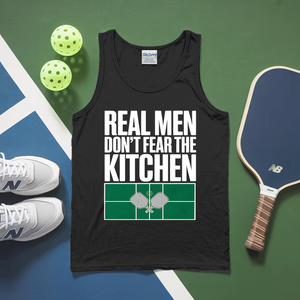Black tank top with 'Real men don't fear the kitchen' text, pickleball paddles, and balls on a green and blue background.