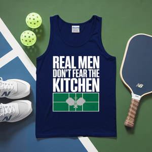 Navy tank top with 'Real men don't fear the kitchen' text on a sports court background with pickleball equipment.