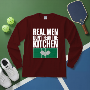 Maroon long-sleeve shirt with text on a green and blue surface with pickleball equipment.