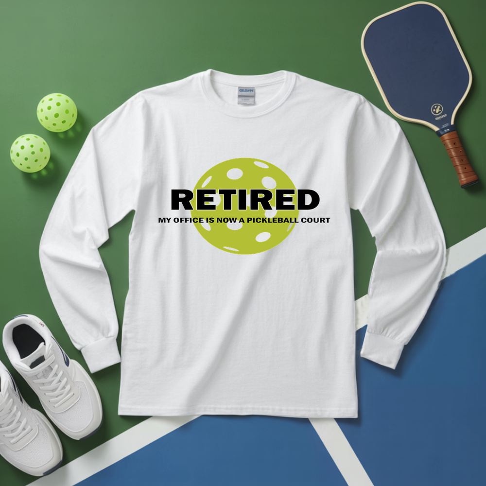 White long-sleeve shirt with pickleball-themed design on a green and blue surface with pickleball equipment.