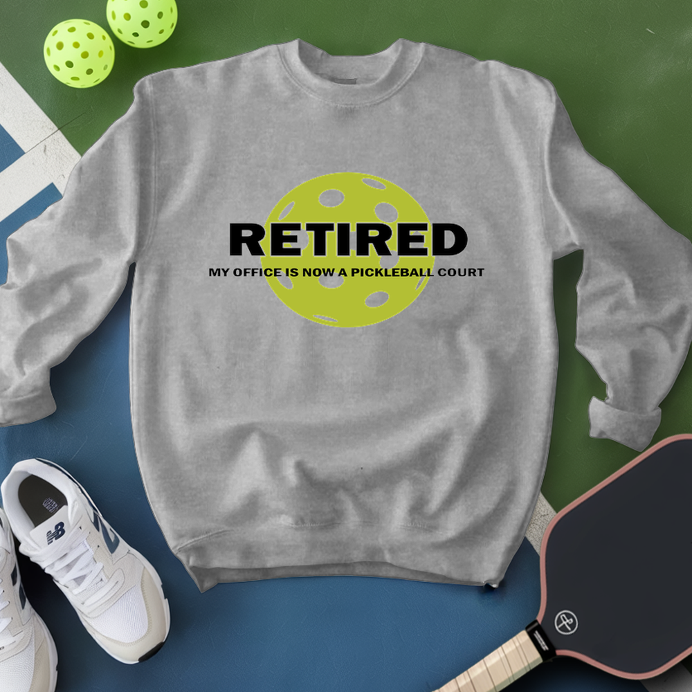 Gray sweatshirt with 'RETired' graphic and pickleball accessories on a green and blue background